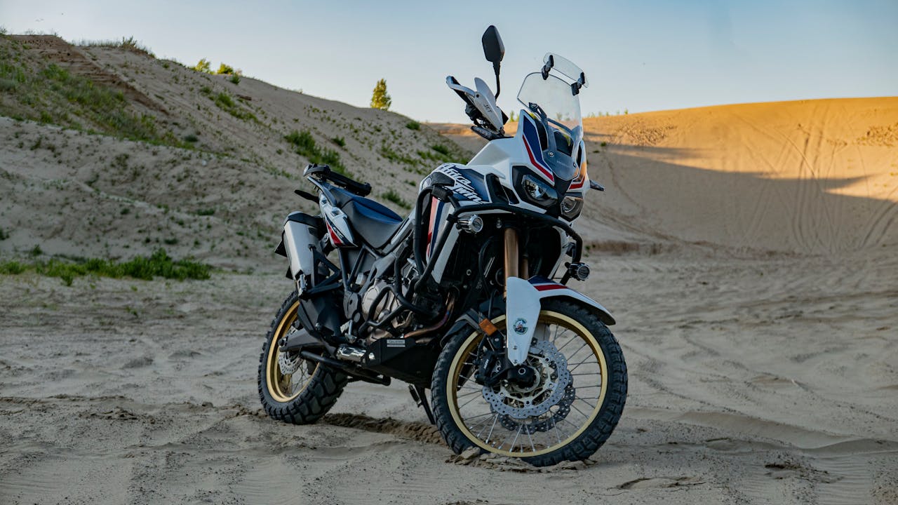 Home A rugged adventure motorcycle parked on expansive desert sand dunes, captured at daylight.