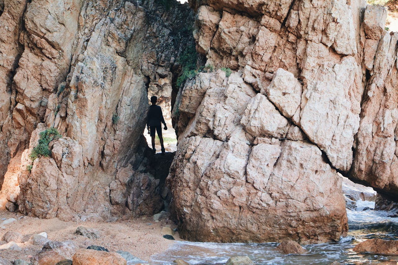 gallery-04 Silhouette of a person exploring a rocky coastal cave formation, capturing adventure in nature.