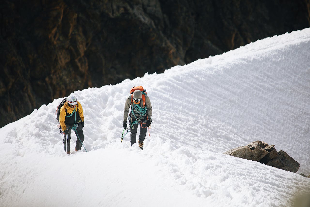 Home Two climbers navigate a snowy ridge, showcasing winter adventure and teamwork.