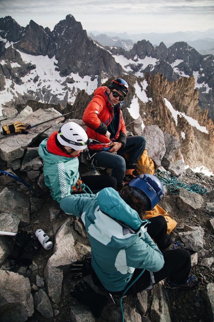 pexels photo 18331844 Three climbers pause on a snowy mountain peak, equipped with gear, surrounded by rugged alpine terrain.